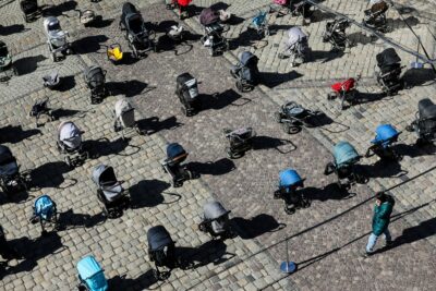 شخصی به 109 کالسکه خالی که در مرکز شهر لویو اوکراین در جریان کمپین "قیمت جنگ" که توسط فعالان و مقامات محلی برای برجسته کردن تعداد کودکان کشته شده در تهاجم روسیه به اوکراین سازماندهی شده نگاه میکند. 18 مارس 2022