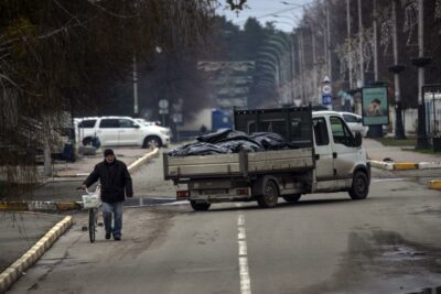 مردی با دوچرخه در بوچا از کنار کامیونی حامل کیسه‌های سیاه محتوی اجساد افرادی که در طول جنگ کشته شده و از یک گور دسته جمعی برای تحقیقات بیرون آورده شده‌اند، عبور میکند. دوشنبه 11 آوریل 2022.
